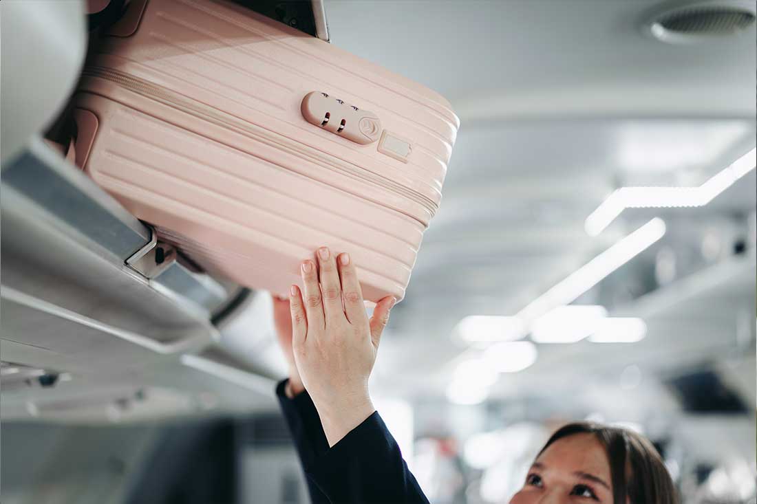 Frau verstaut Handgepäck im Flugzeug.